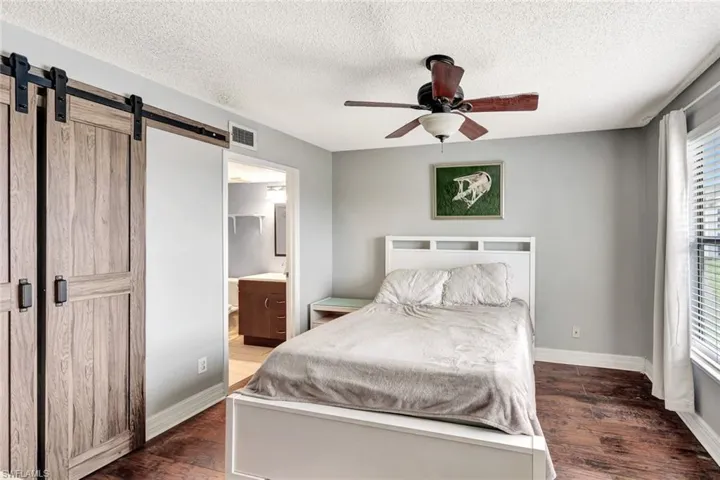 Bedroom featuring ceiling fan, dark hardwood / wood-style flooring, ensuite bath, and a barn door