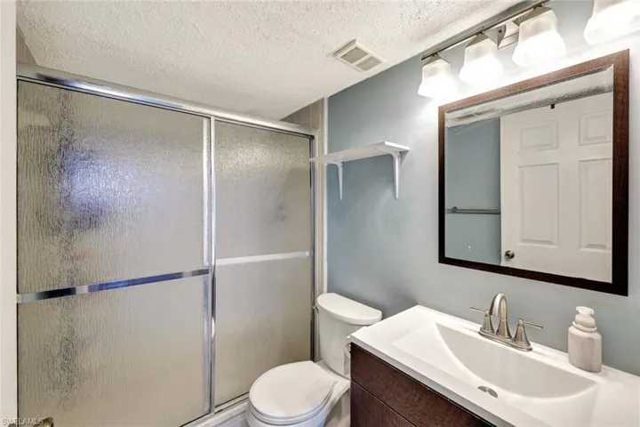 Bathroom featuring a textured ceiling, an enclosed shower, vanity, and toilet