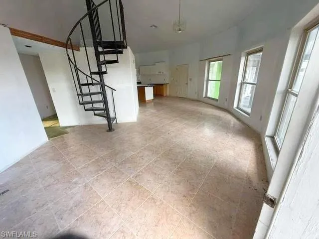 Open-concept living space featuring a spiral staircase, tile flooring, multiple windows, and a partial kitchen area with wood-finish cabinetry