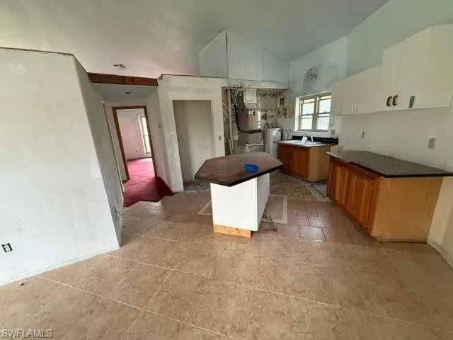 Kitchen featuring an island with a dark countertop, white upper cabinetry, light wood-finish lower cabinetry, and tiled flooring