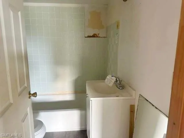 Bathroom featuring a white bathtub, light green tiled shower surround, white vanity with integrated sink, and wood-finish flooring