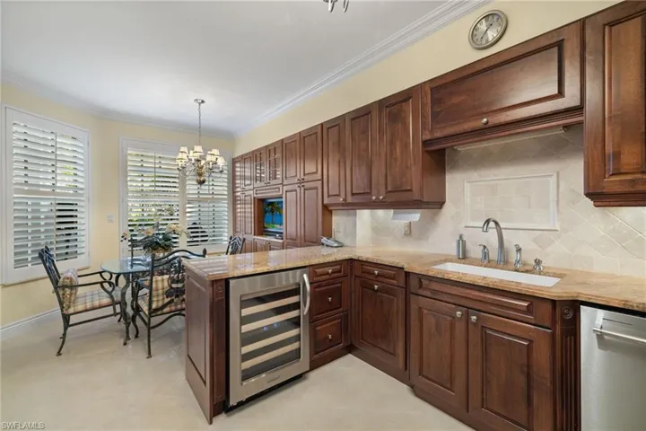 Kitchen featuring ornamental molding, a peninsula, wine cooler, tasteful backsplash, and light stone counters