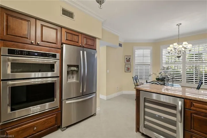 Kitchen with appliances with stainless steel finishes, beverage cooler, ornamental molding, a chandelier, and light stone countertops