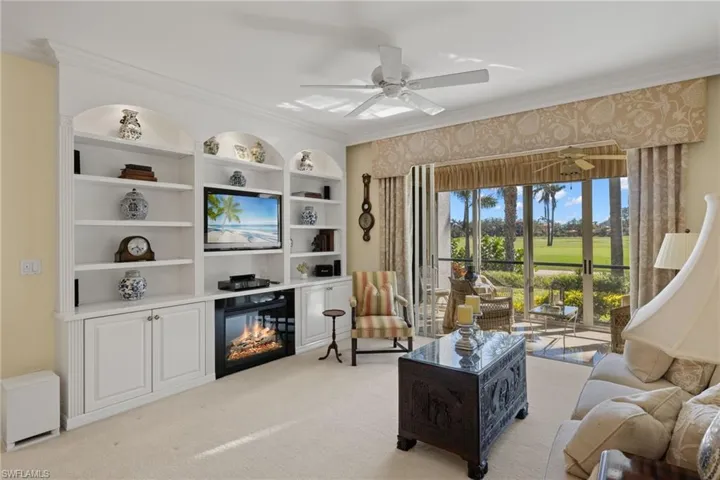 Living area with crown molding, light carpet, a glass covered fireplace, a ceiling fan, and built in shelves