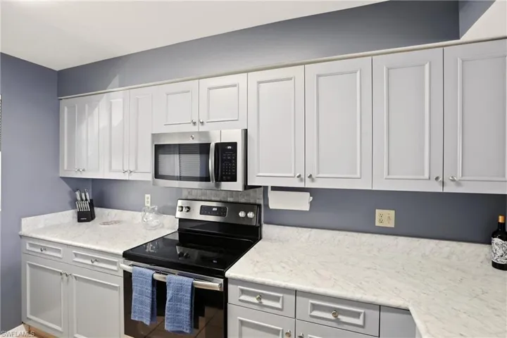 Kitchen featuring stainless steel appliances, white cabinets, and light stone countertops