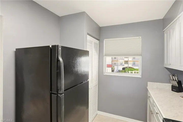 Kitchen with freestanding refrigerator, white cabinetry, and light tile patterned floors