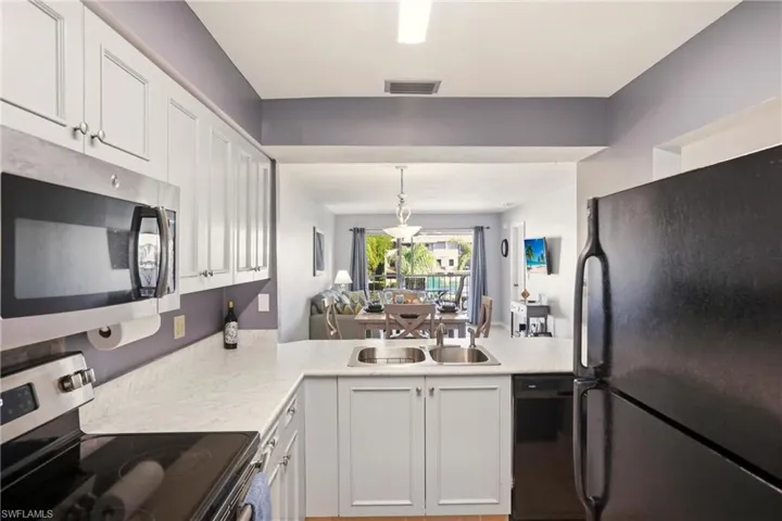 Kitchen featuring black appliances, white cabinetry, light countertops, hanging light fixtures, and open floor plan
