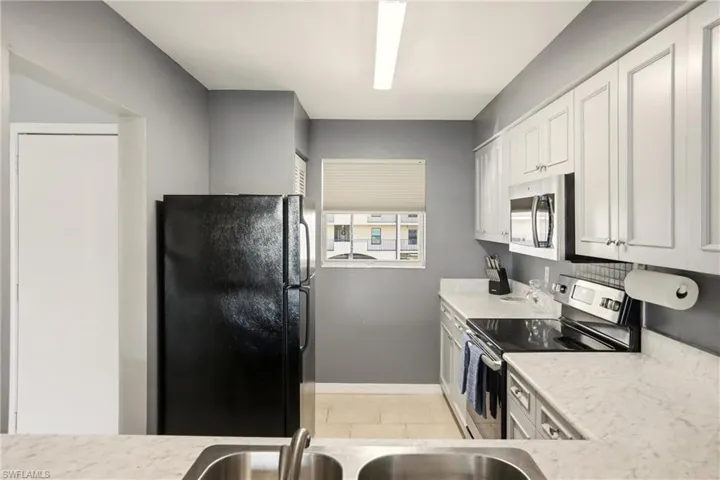 Kitchen with appliances with stainless steel finishes, white cabinets, and light tile patterned flooring