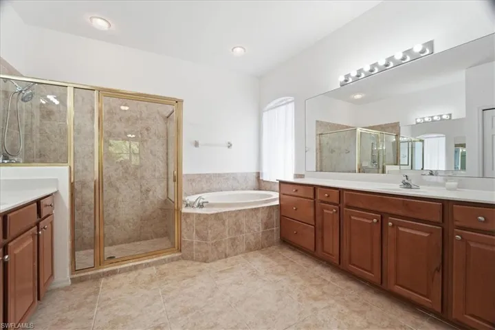 Full bath featuring dual vanities, a garden tub, a shower stall, and private WC