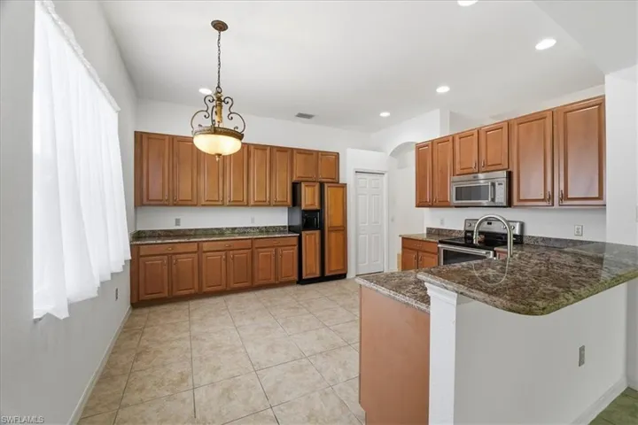 Eat in kitchen featuring wood cabinetry, arched walkways, stainless steel appliances, hanging light fixtures, and recessed lighting
