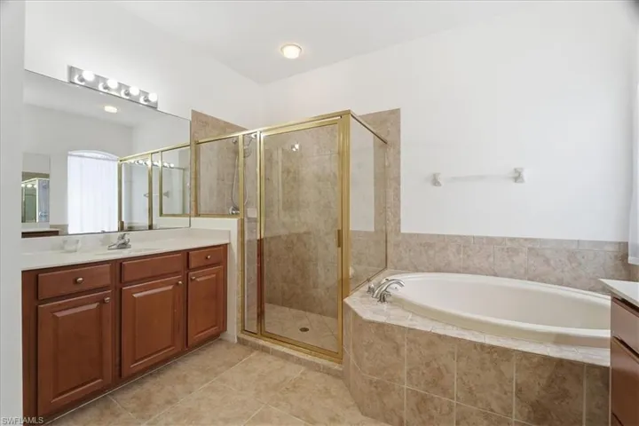 Full bath featuring dual vanities, a garden tub, a shower stall, and private WC