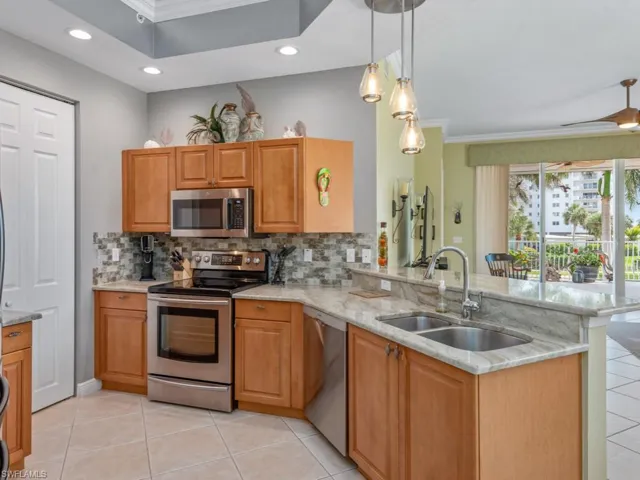 Kitchen with a peninsula, stainless steel appliances, a sink, light stone counters, and backsplash