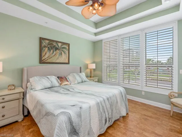 Bedroom with a ceiling fan, a tray ceiling, baseboards, and wood finished floors
