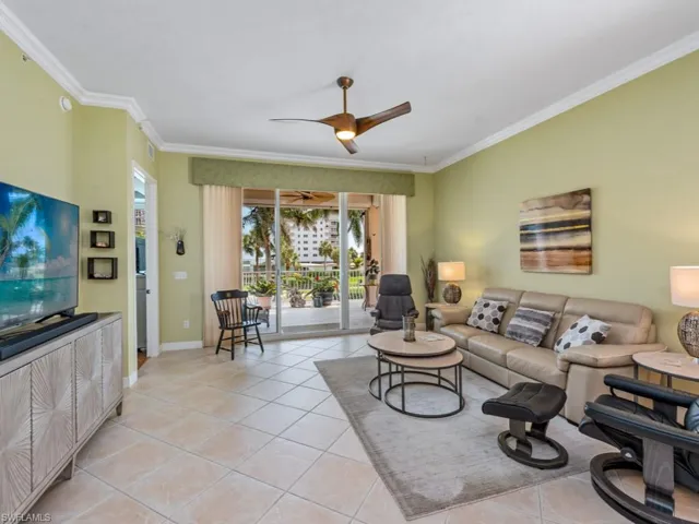 Living area featuring light tile patterned flooring, baseboards, crown molding, and a ceiling fan
