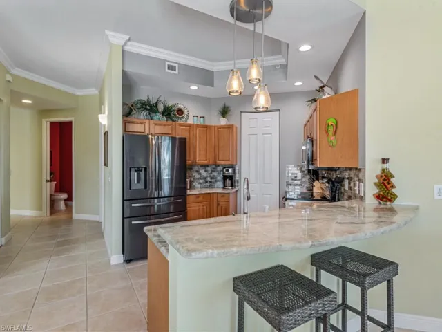Kitchen with refrigerator with ice dispenser, a peninsula, brown cabinets, light tile patterned floors, and visible vents