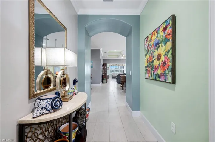 Tiled hallway featuring an arched entryway, crown molding, and light-toned walls