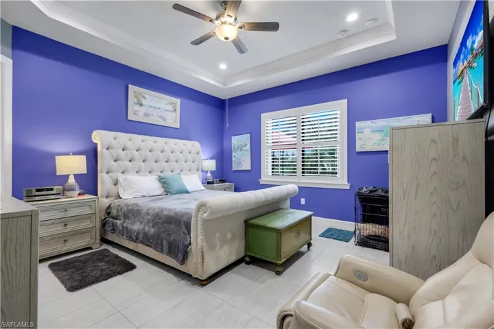 Spacious Primary Bedroom featuring vibrant walls, a tray ceiling with recessed lighting and a ceiling fan, with plantation shutters