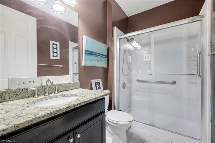 Bathroom featuring a dark wood-finish vanity with a granite countertop and undermount sink, a chrome faucet, and a glass-enclosed shower with grab bars and a white tile floor