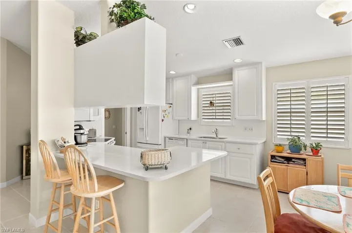 Kitchen with kitchen peninsula, a kitchen bar, white appliances, and white cabinets