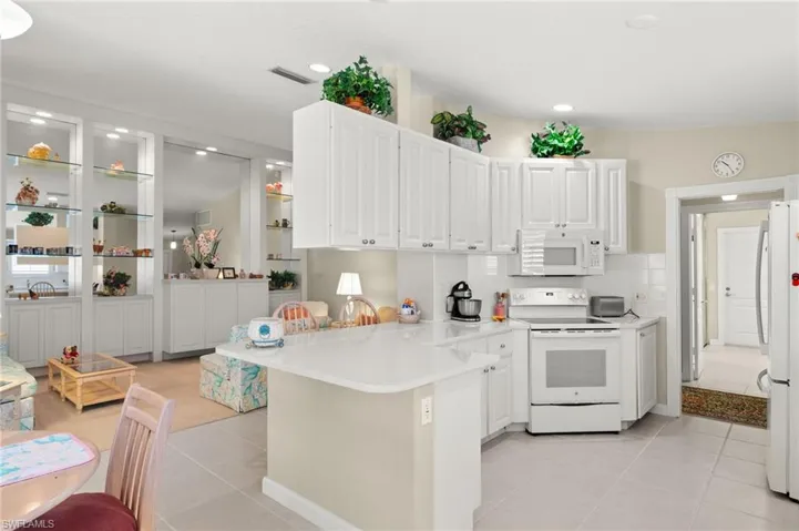 Kitchen with white appliances, light tile patterned floors, kitchen peninsula, and white cabinetry