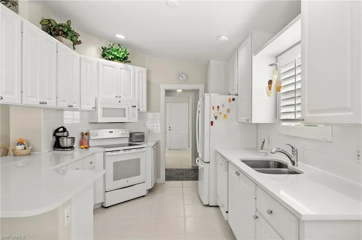 Kitchen with tasteful backsplash, white appliances, sink, light tile patterned floors, and white cabinetry