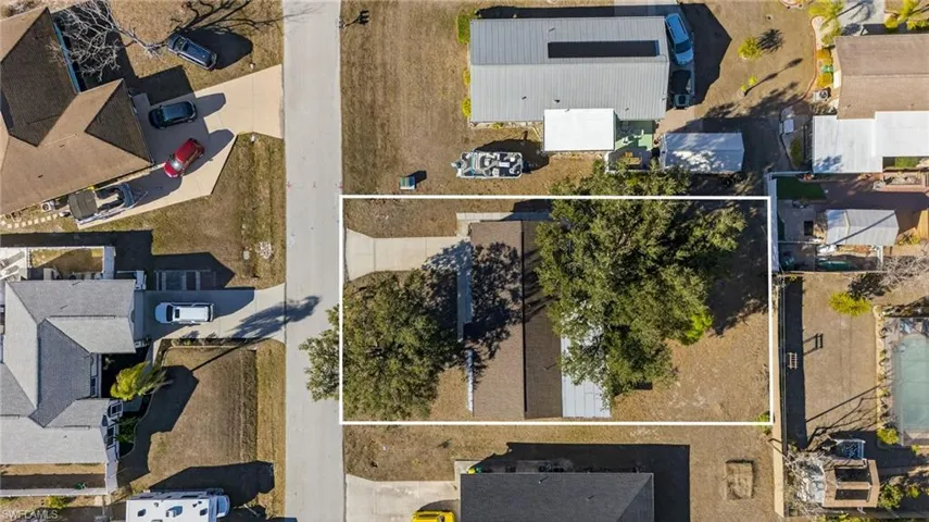 Aerial perspective of a rectangular lot featuring mature trees, a concrete driveway, and a multi-sectioned roof structure
