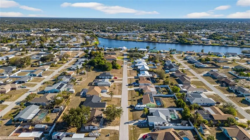 Aerial perspective of a residential neighborhood featuring paved streets, mature trees, and proximity to a canal