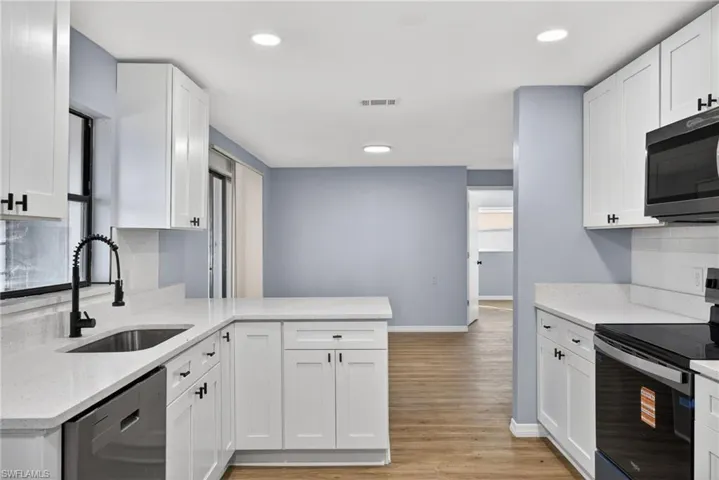 Kitchen featuring white Shaker-style cabinetry, light-toned countertops, wood-finish flooring, recessed lighting, and a matte black gooseneck faucet