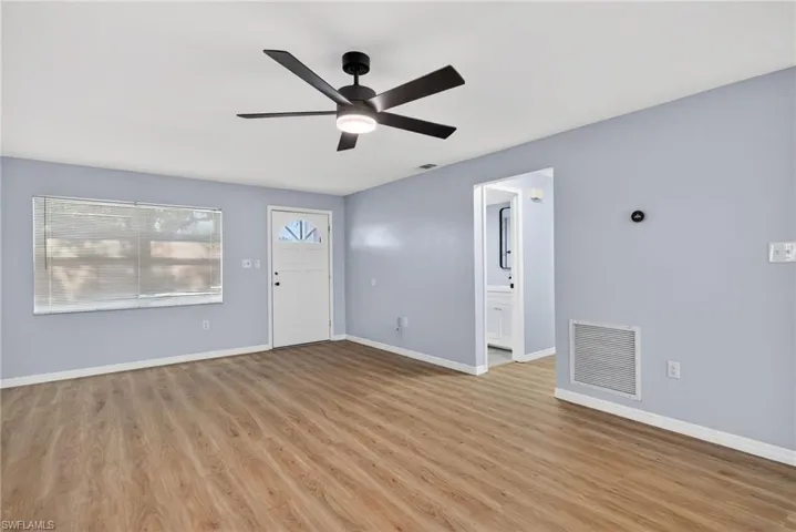 Light-filled interior featuring wood-finish flooring, a matte black five-blade ceiling fan with integrated lighting, a multi-pane entry door, and neutral wall tones