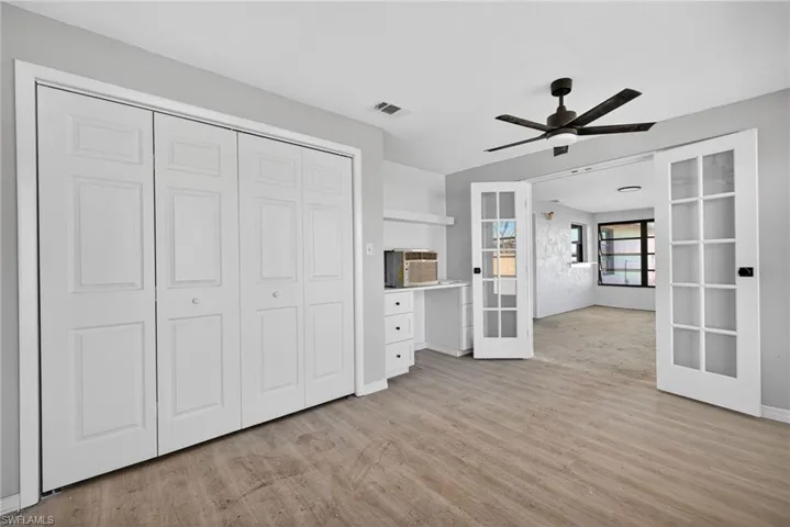 Interior space featuring wood-finish flooring, floor-to-ceiling multi-panel folding closet doors, white built-in cabinetry with a desk surface, a multi-light ceiling fan, and white French doors with glass panes