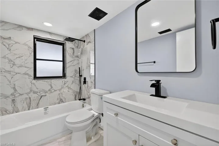 Bathroom featuring white vanity with integrated basin, matte black faucet, rectangular mirror with black frame, and full-height wall tiling surrounding the tub