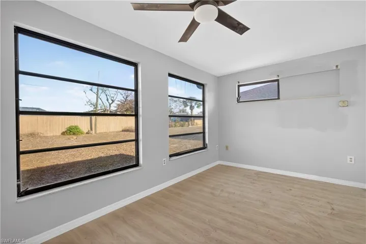 Room featuring wood-finish flooring, three horizontal windows with black framing, and a ceiling-mounted fan with integrated lighting
