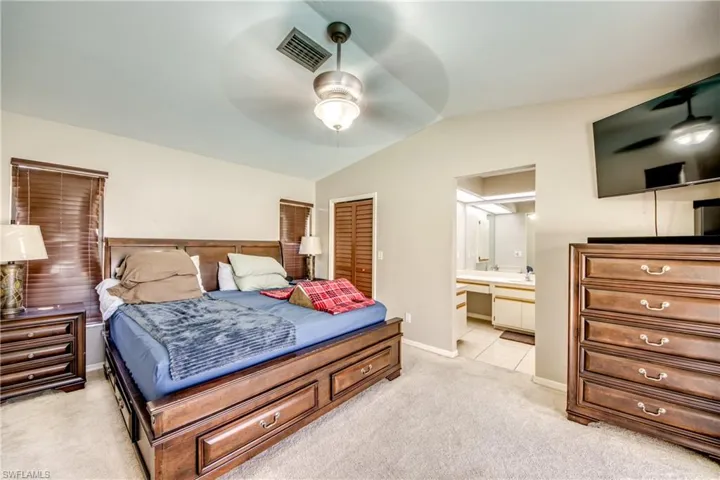 Bedroom featuring light carpet, vaulted ceiling, a closet, a ceiling fan, and ensuite bath