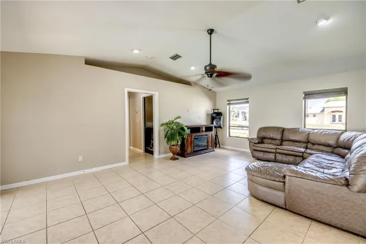 Living area with light tile patterned floors, vaulted ceiling, a glass covered fireplace, a ceiling fan, and recessed lighting