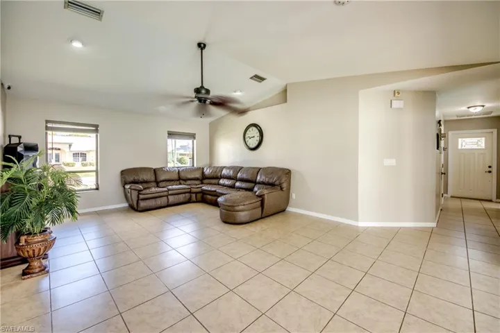 Living room with light tile patterned floors, lofted ceiling, ceiling fan, and recessed lighting