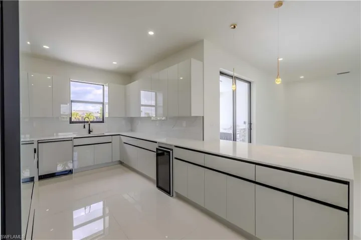 Kitchen with white dishwasher, wine cooler, modern cabinets, tasteful backsplash, and white cabinetry