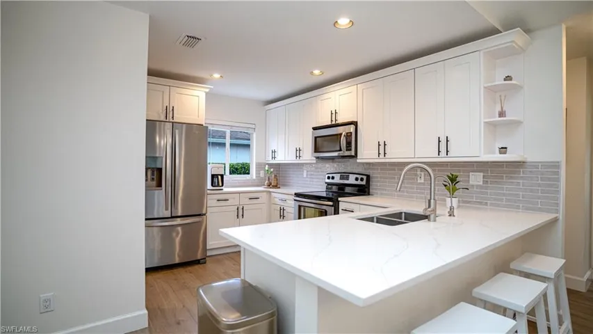 Kitchen with appliances with stainless steel finishes, white cabinets, open shelves, decorative backsplash, and light wood-style floors