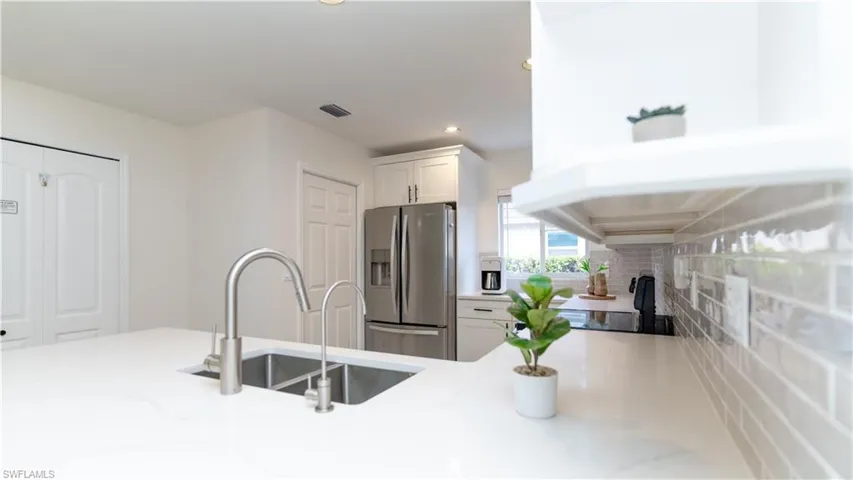 Kitchen with stainless steel fridge with ice dispenser, white cabinetry, light stone counters, recessed lighting, and black electric range oven
