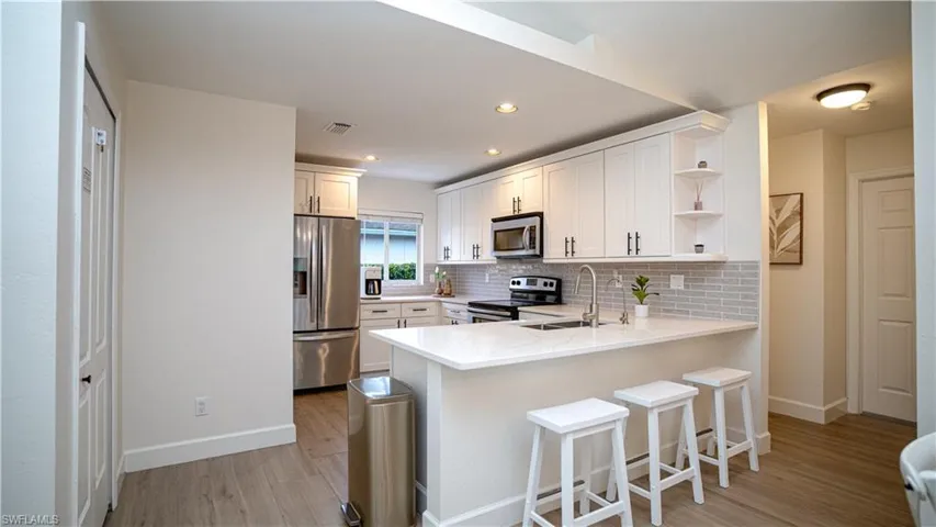 Kitchen with white cabinetry, appliances with stainless steel finishes, tasteful backsplash, light wood-style flooring, and a kitchen bar
