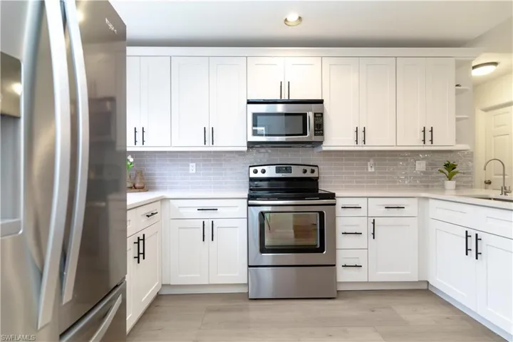 Kitchen with stainless steel appliances, white cabinetry, open shelves, light stone counters, and backsplash