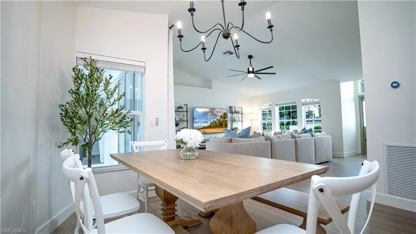 Dining area with wood finished floors, a chandelier, ceiling fan, and high vaulted ceiling