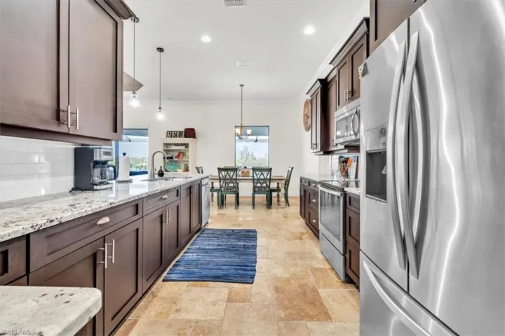Galley kitchen featuring dark wood cabinetry, light-toned granite countertops, and a subway tile backsplash