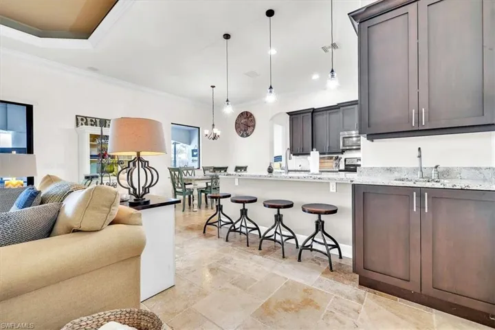 Open-concept living space featuring light-toned tile flooring, tray ceiling, dark wood cabinetry, light-toned countertops, and a kitchen island with pendant lighting
