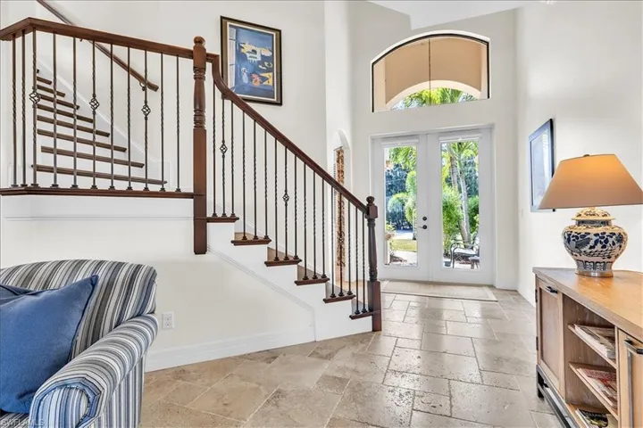 Two-story entry foyer featuring a grand staircase with wrought iron balusters and wood handrails, double-door entry with an arched transom, and stone tile flooring
