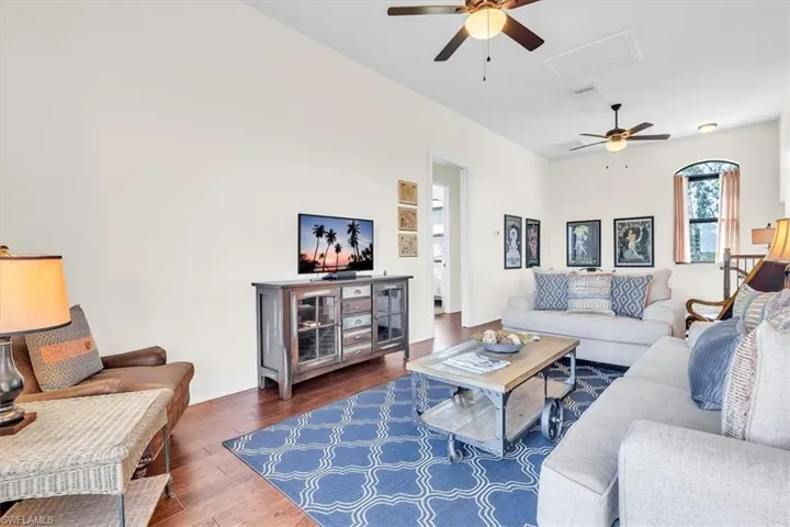 Spacious living area featuring high vaulted ceilings, multiple ceiling fans with integrated lighting, wood-finish flooring, a decorative arched window, and a built-in media console