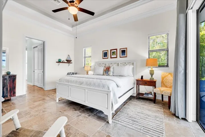 Spacious bedroom featuring large format tile flooring, crown molding, and a tray ceiling with a ceiling fan