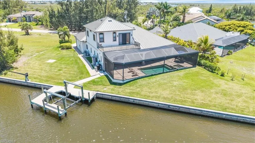 Waterfront property featuring a private boat dock with lift, screened pool enclosure, expansive pool deck, upper-level balcony, and mature landscaping