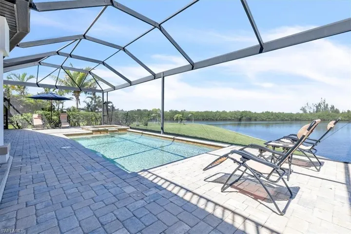 Screened lanai featuring a swimming pool, integrated spa, and paver decking overlooking a body of water