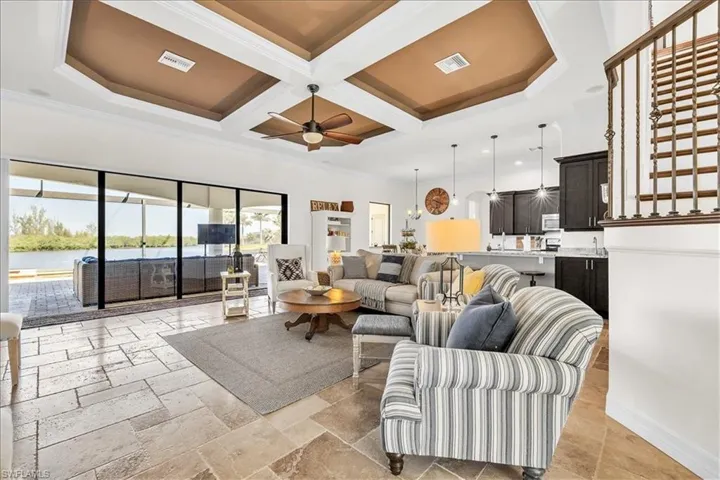 Spacious living area featuring coffered ceilings, large format tile flooring, and sliding glass doors leading to an outdoor living space