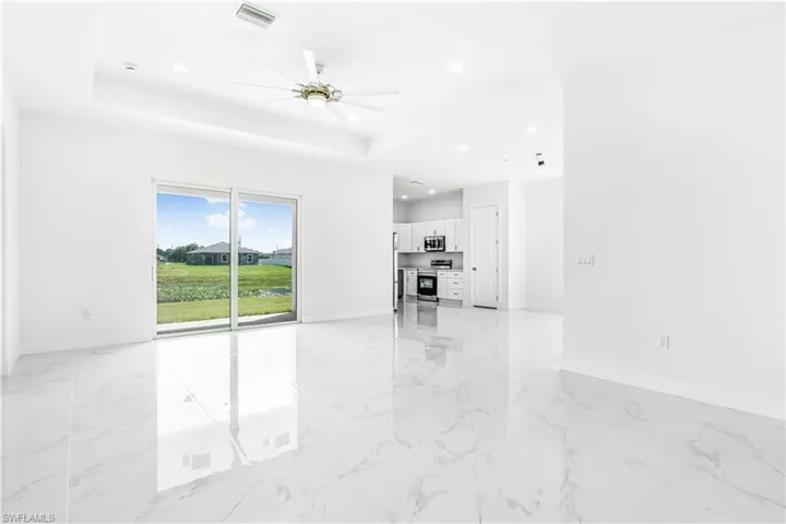 Unfurnished living room with ceiling fan, light tile patterned flooring, and a tray ceiling